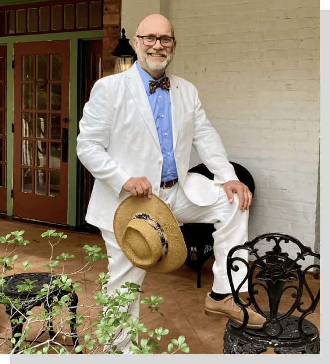A man in white suit and hat holding his hat.